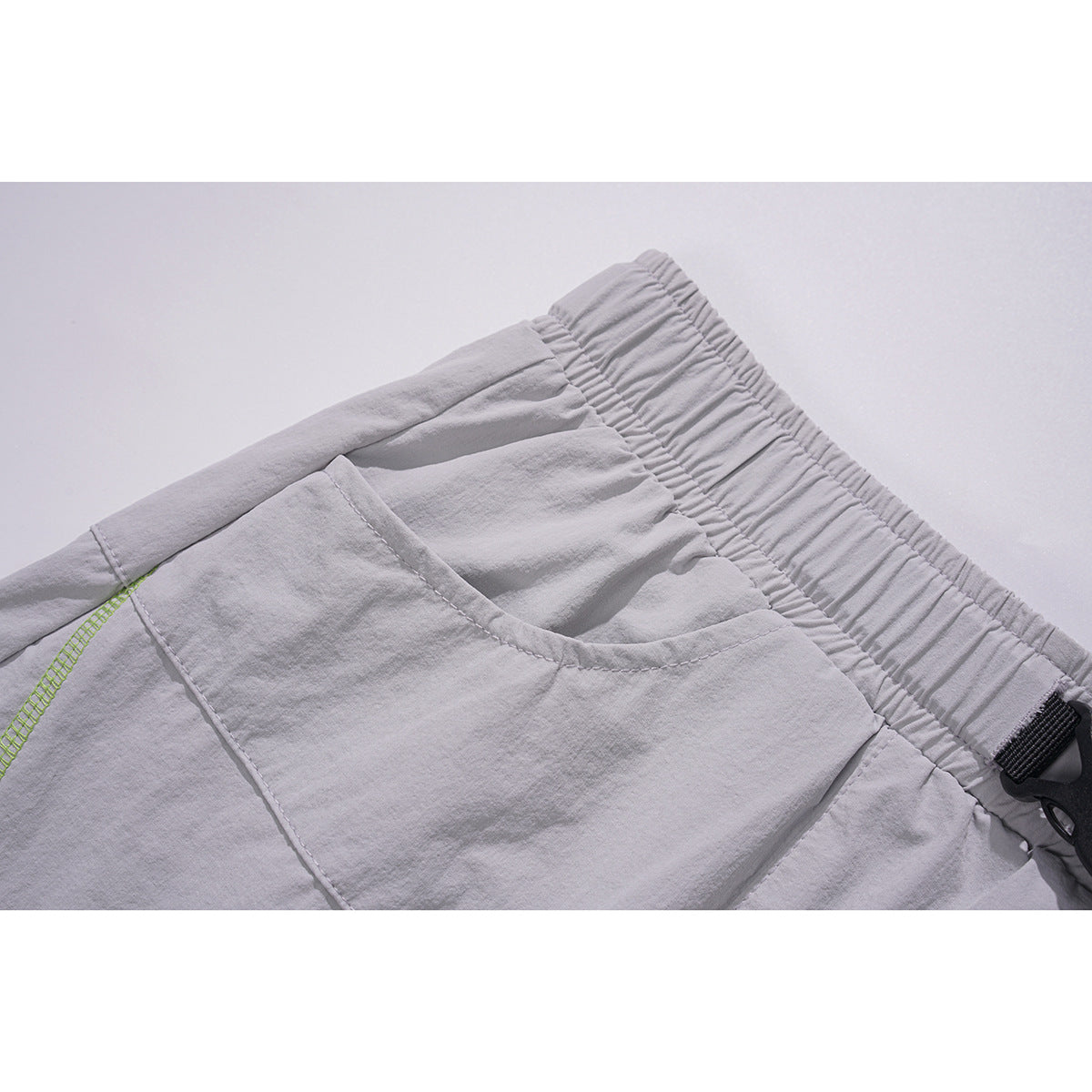Close-up of light gray shorts showing the elastic waistband and curved pocket with lime-green stitching inside.