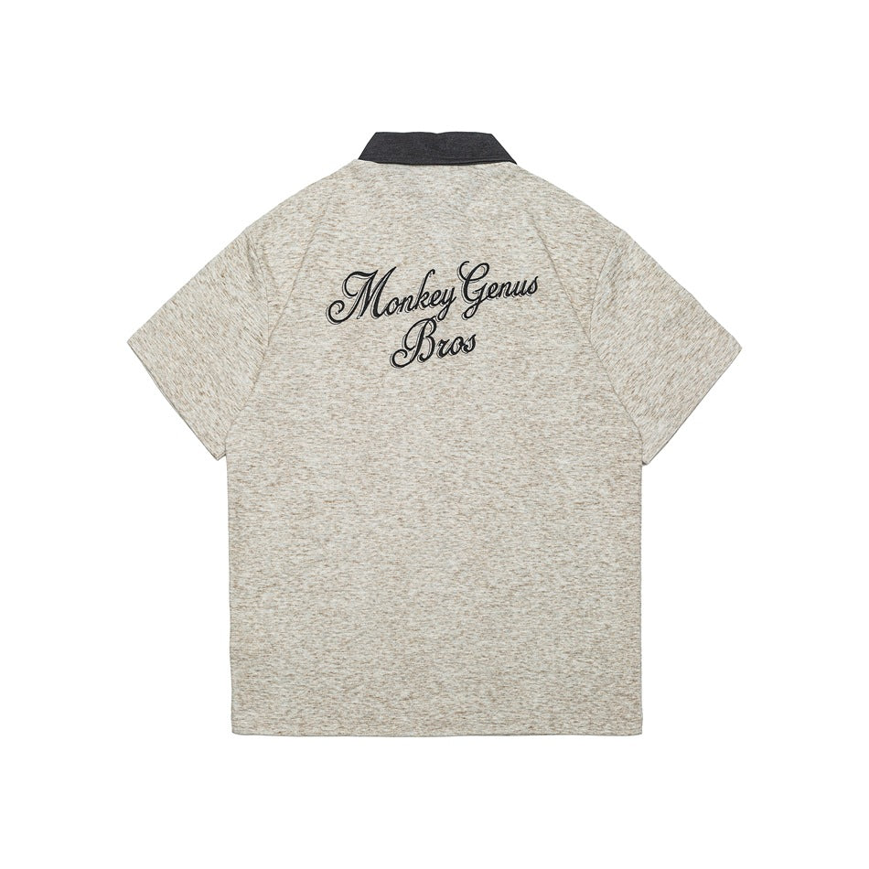 Back of beige heather gray polo shirt with large black script embroidery across the upper back and dark gray collar