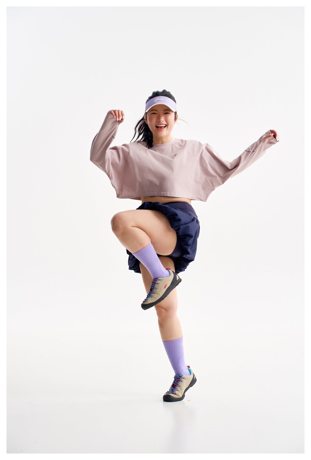 Model poses in a pale pink cropped long-sleeve top and navy bubble-hem skirt, lifting one knee.