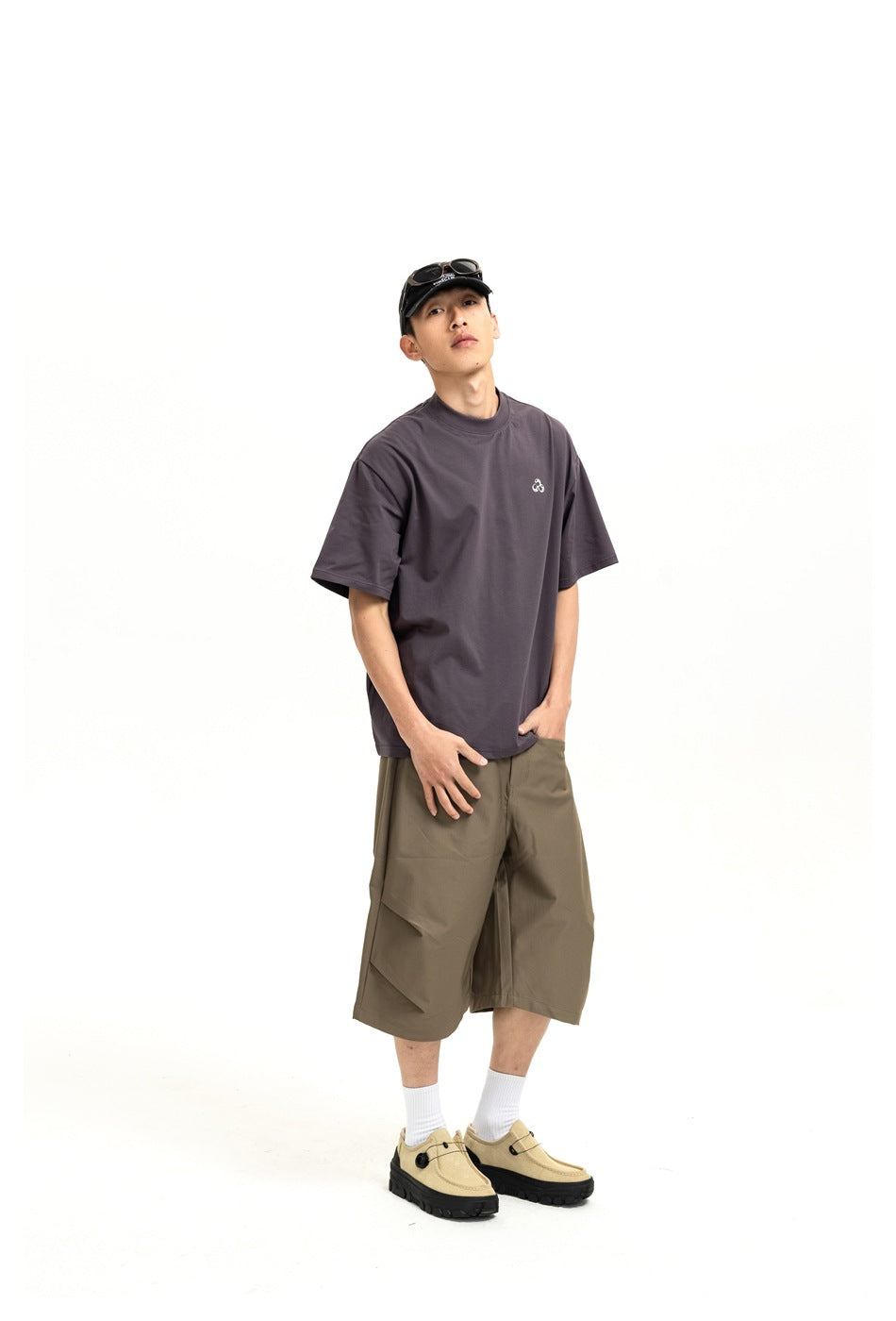 Model in a charcoal oversized T-shirt with a small chest emblem and olive knee-length shorts, shown at an angle.