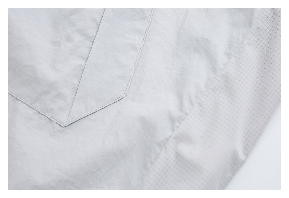 Close-up of a light gray garment panel with angular stitching and a contrasting fine grid-patterned section.