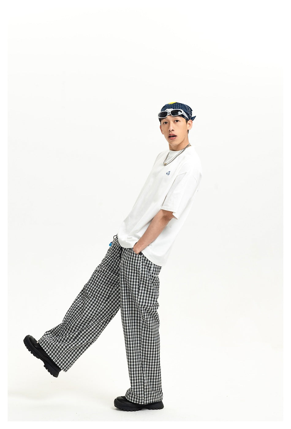 Person wearing white short-sleeve T-shirt with small chest logo, checked wide-leg pants and bandana, posed side-on