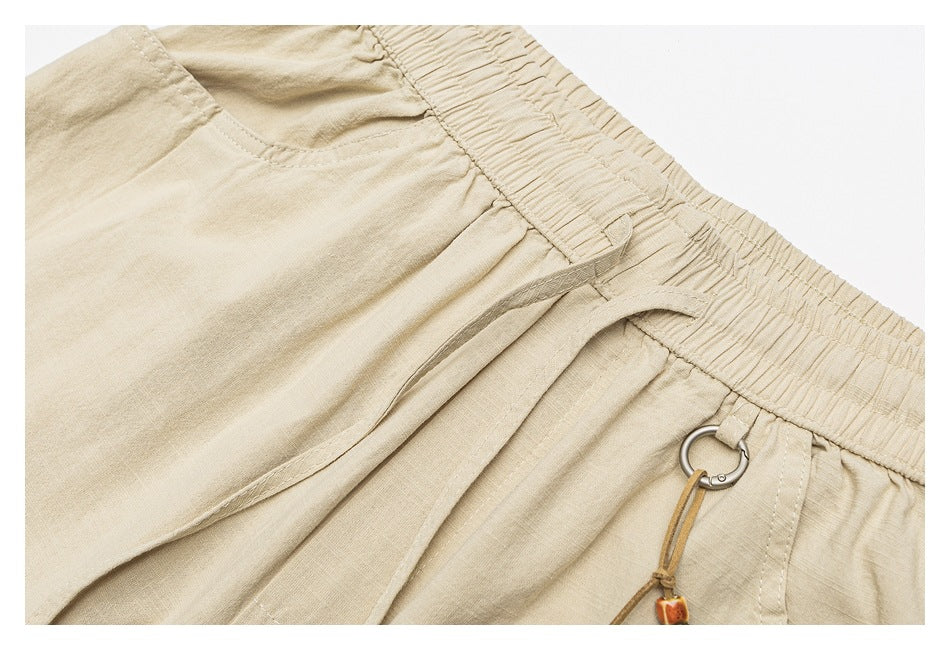 Close-up of beige bottoms showing an elastic waistband, pocket opening, and a cord charm attached to a metal ring.