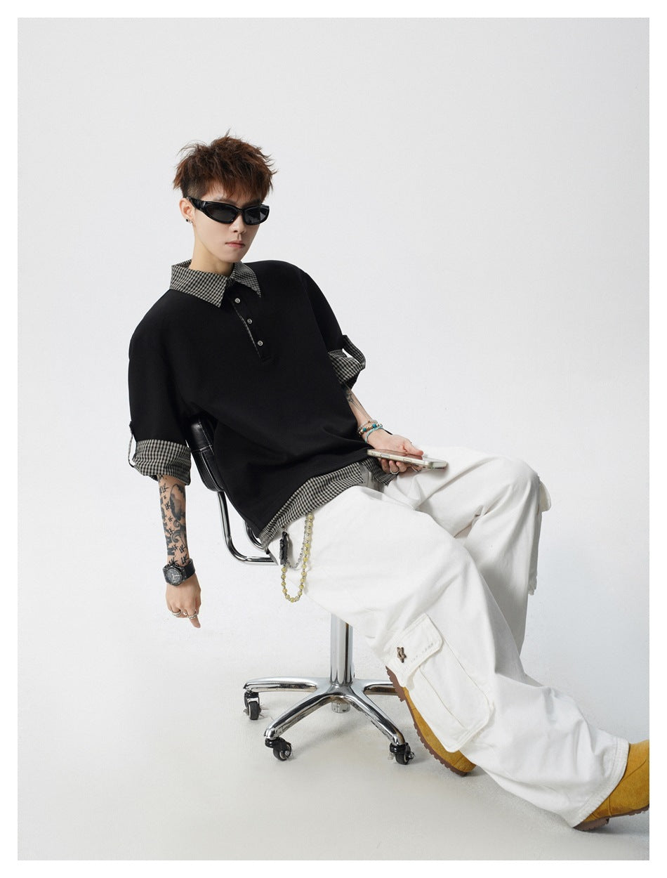 Model reclining in a black polo with checked collar, cuffs and hem, paired with loose white trousers.