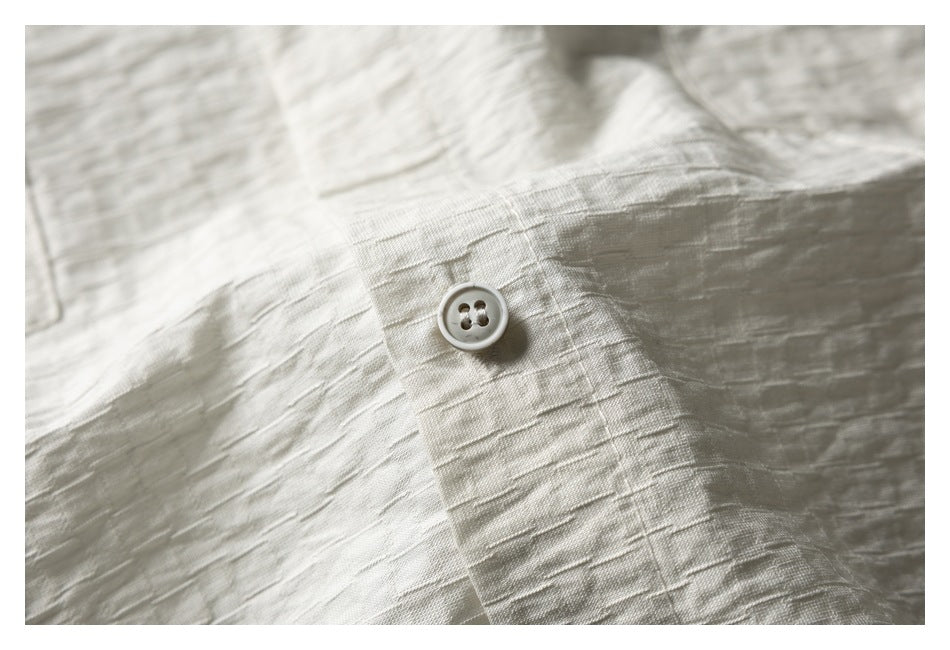 Close-up of a light button on pale ivory textured fabric with visible stitching.