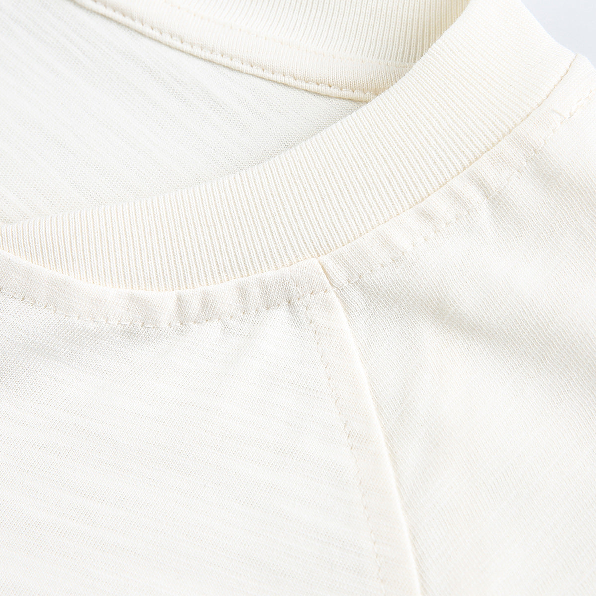 Close-up of an ivory T-shirt's ribbed crew neckline, shoulder seam, and stitching.