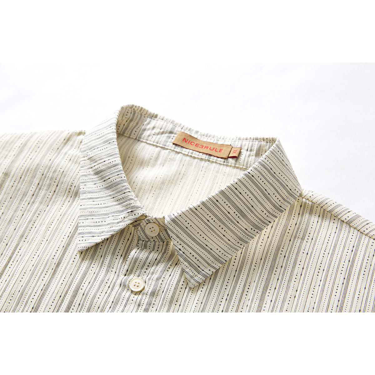 Close-up of an ivory button-up shirt with fine black dotted stripes, pointed collar, buttons, and a visible neck label.