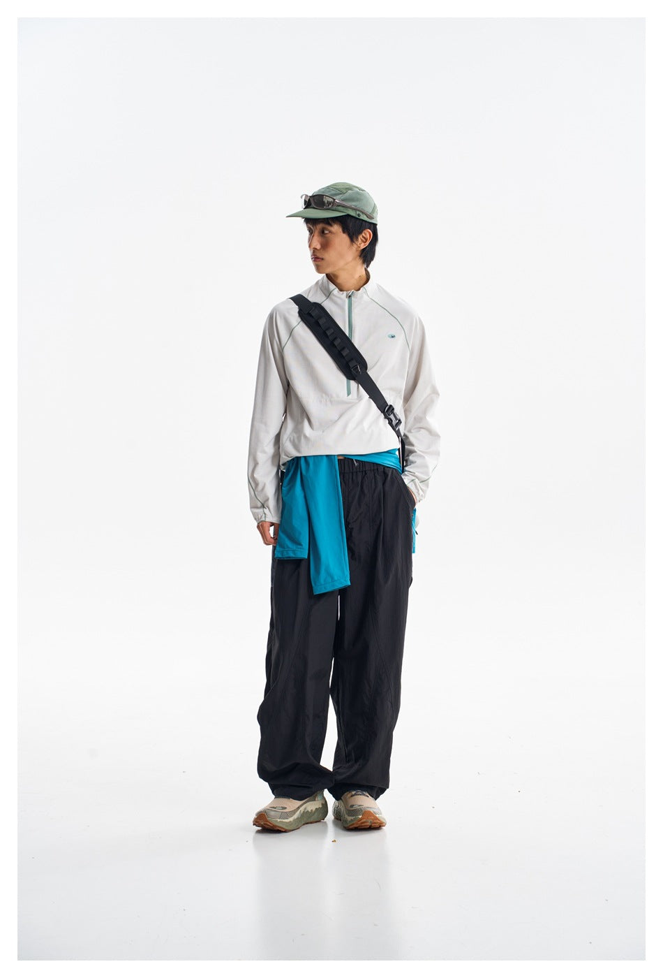 Full-length model wearing a white zip-neck pullover, loose black pants, and a turquoise layer tied at the waist.