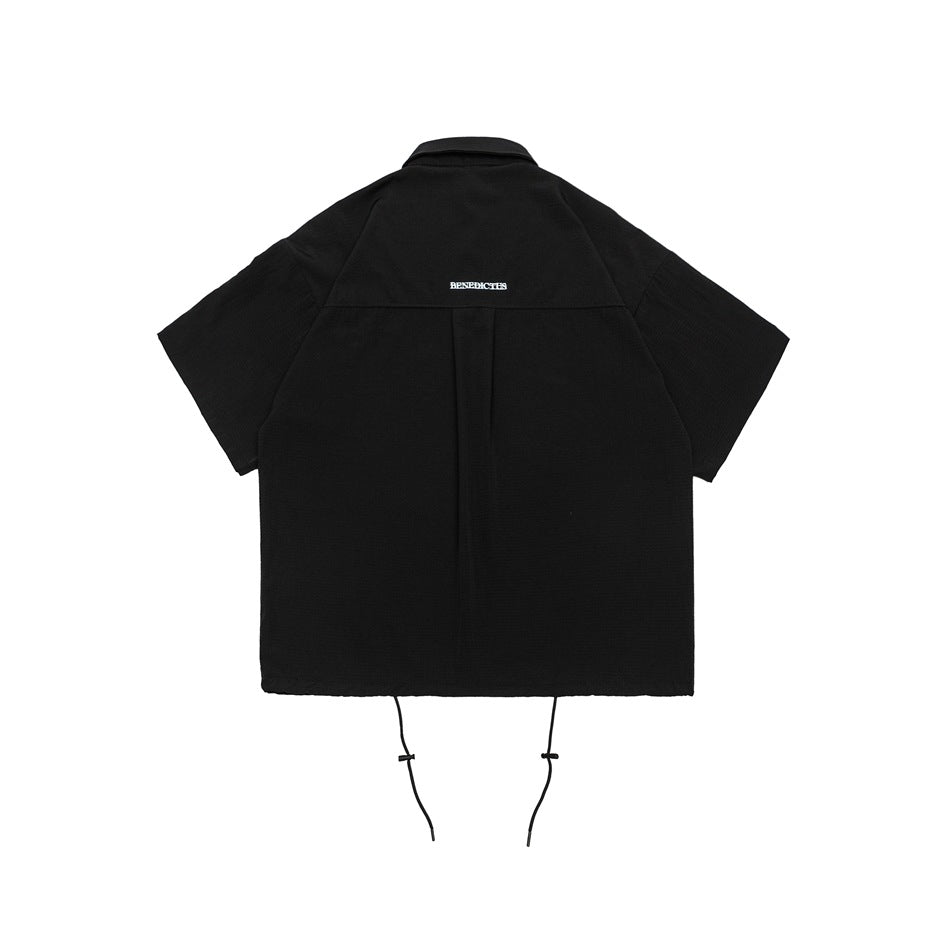 Back view of a black short-sleeve collared shirt with a center pleat and dangling hem cords.