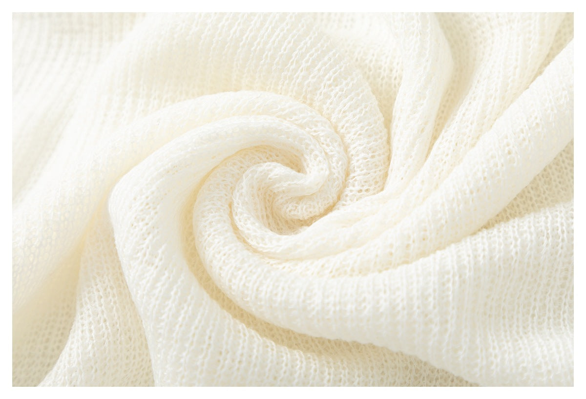 Close-up of ivory open-knit fabric gathered into folds, showing its airy looped texture.