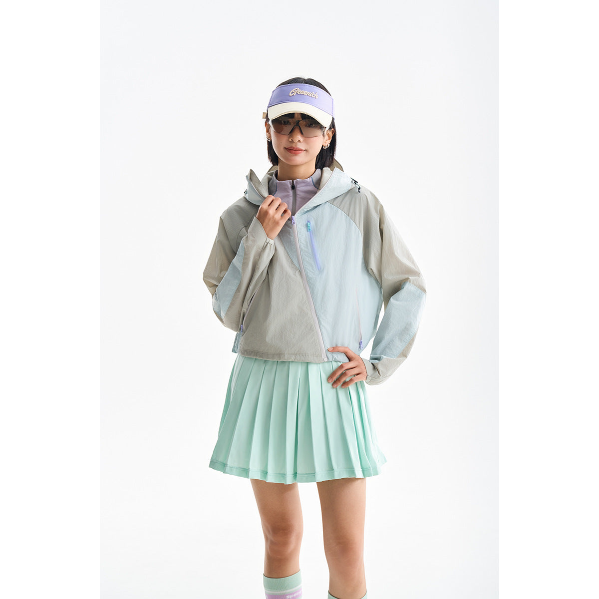 Model wearing a pale gray and mint color-block hooded jacket with a mint pleated skirt.