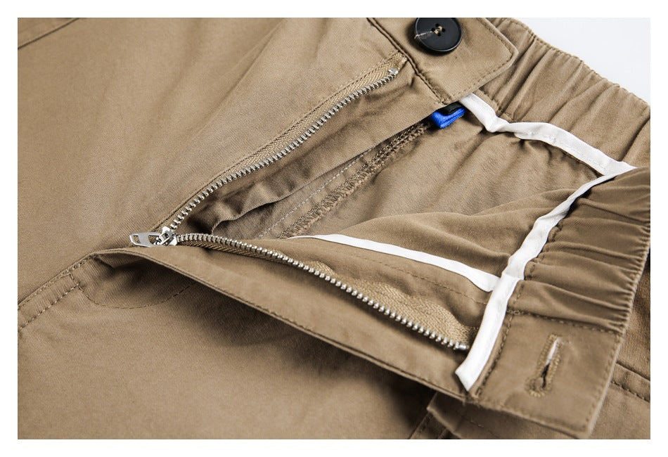 Close-up of tan trousers showing the button, open zip fly, and white inner trim.