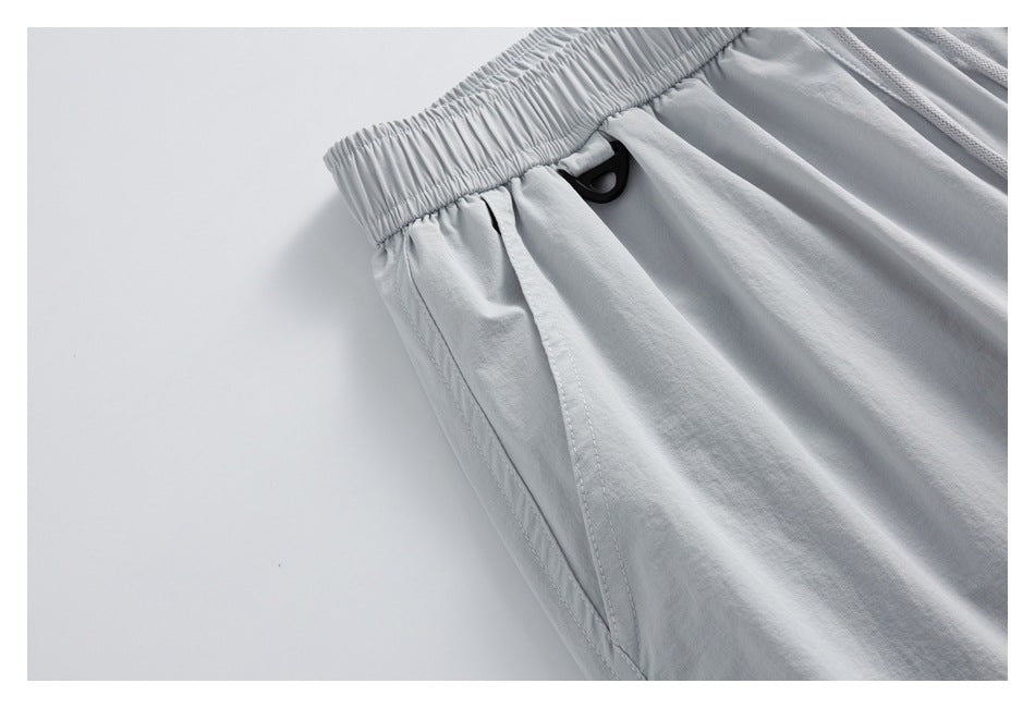 Close-up of light gray shorts showing the gathered elastic waistband, side pocket seam, and black loop detail.