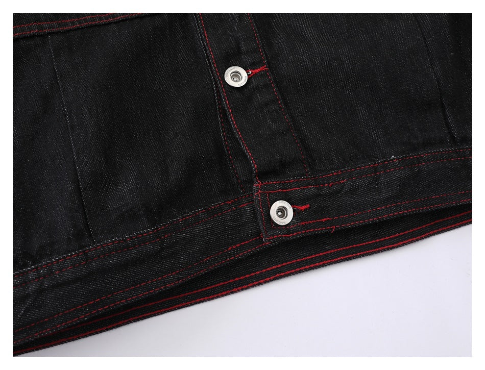 Close-up of the black denim jacket hem and front placket with silver snaps and red stitching.
