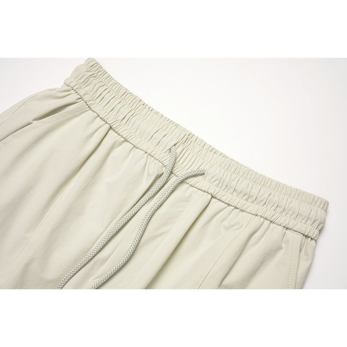 Close-up of off-white pants showing an elastic drawstring waist and stitched front panels.