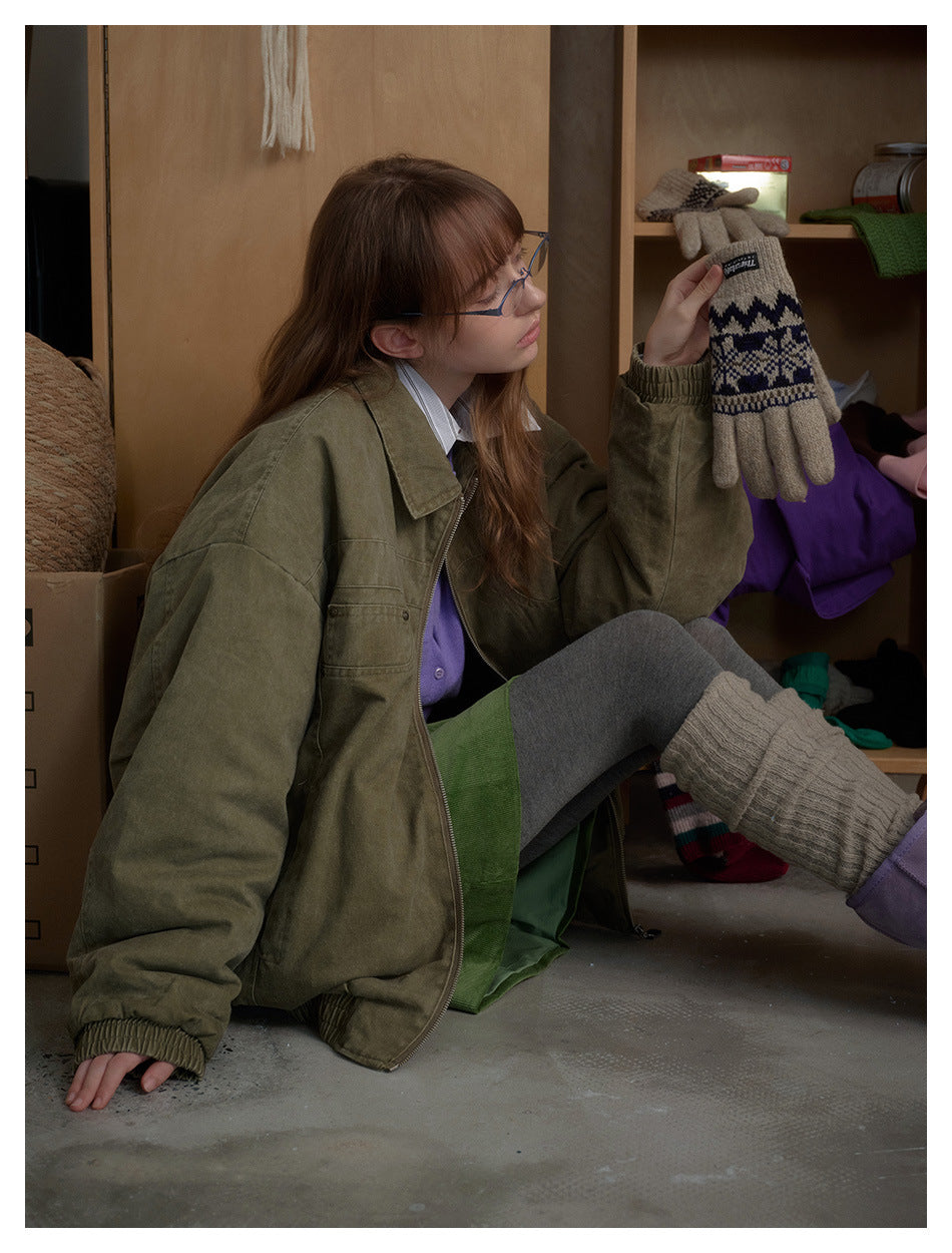 Side view of a seated model wearing an oversized olive jacket with a zip front, wide collar and gathered cuffs.
