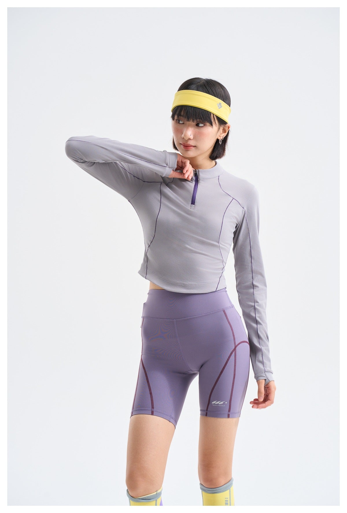 Model wearing a light gray-lavender quarter-zip top and purple fitted shorts with contrast seam lines.