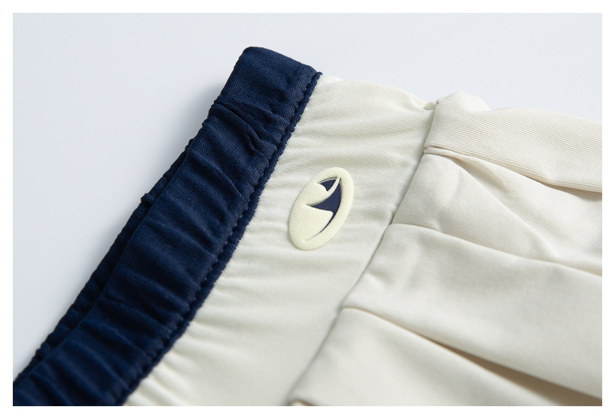 Close-up of a small oval navy-and-cream emblem beside the navy waistband on a cream pleated garment.