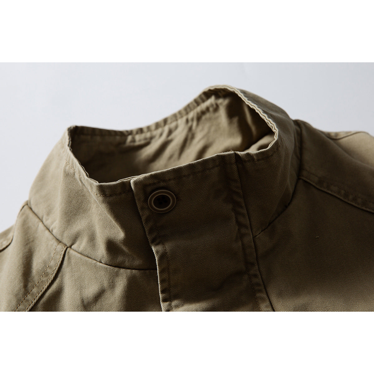 Close-up of an olive-khaki jacket's stand collar, button tab and shoulder seam.