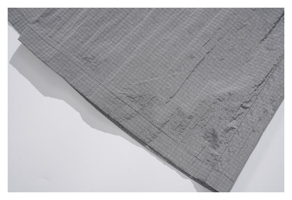 Close-up of stitching along the edge of charcoal-gray fabric with a fine white grid.