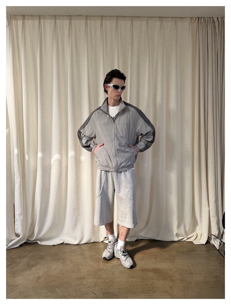 Model wearing a light gray zip-up jacket with dark shoulder stripes, paired with gray shorts.