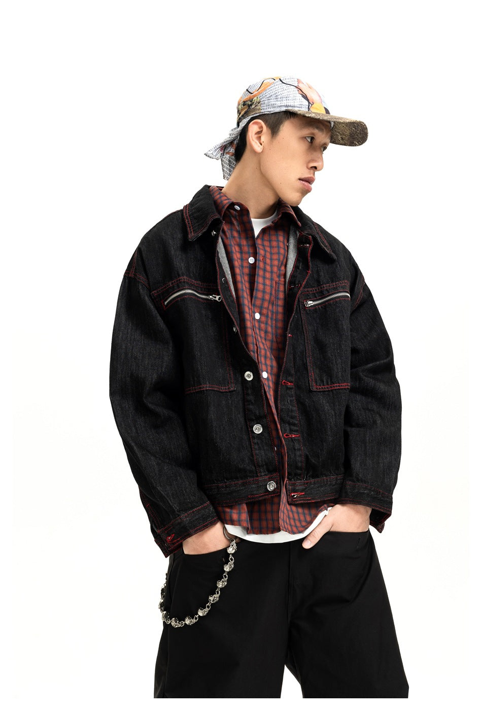 Model wearing a black jacket with red stitching and zippered chest pockets over a red plaid shirt.