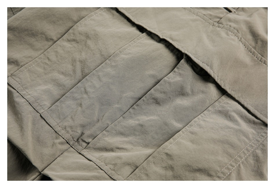 Close-up of a rectangular stitched pocket on olive-gray trousers.