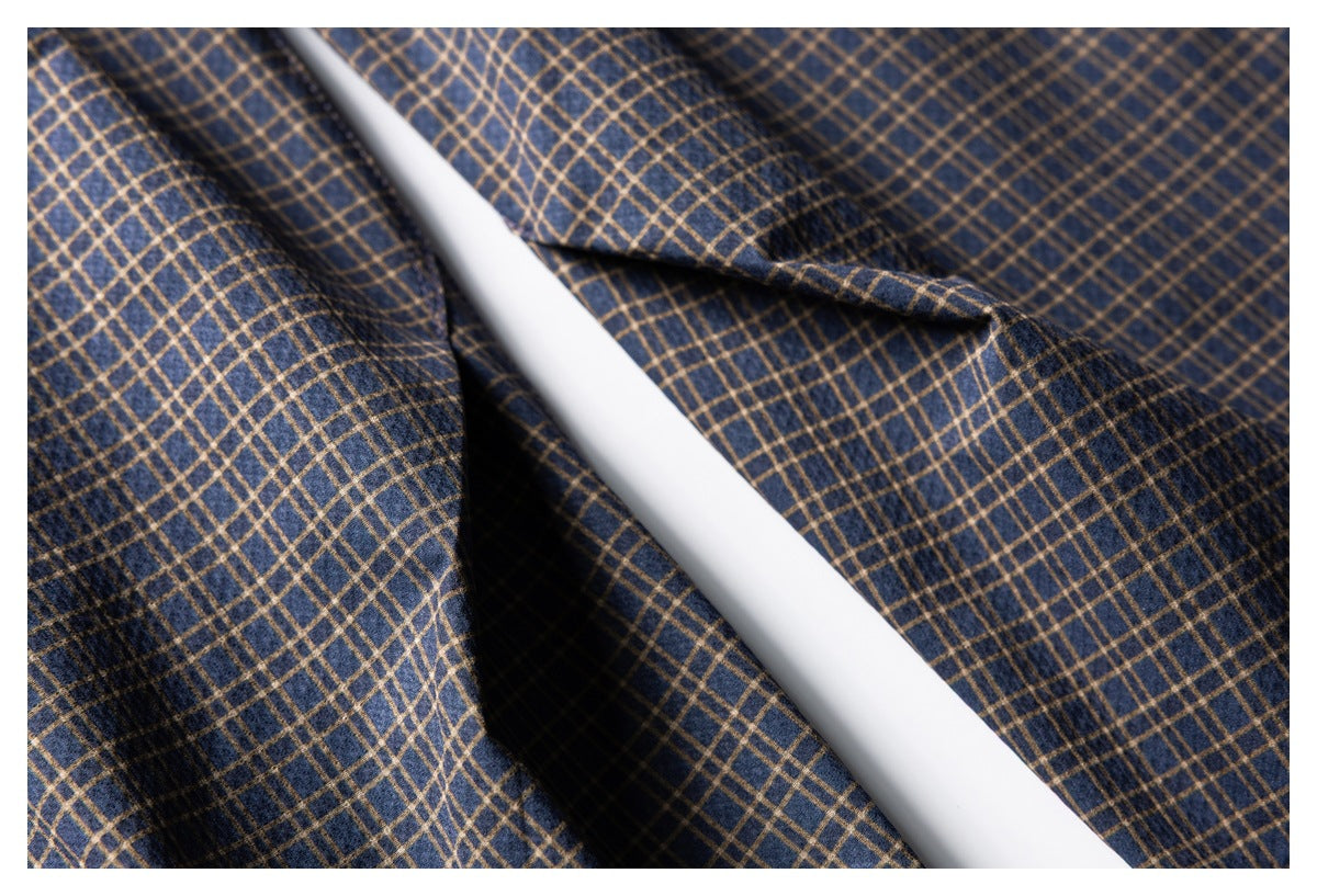 Close-up of navy and tan plaid garment fabric, folds, and a stitched seam.