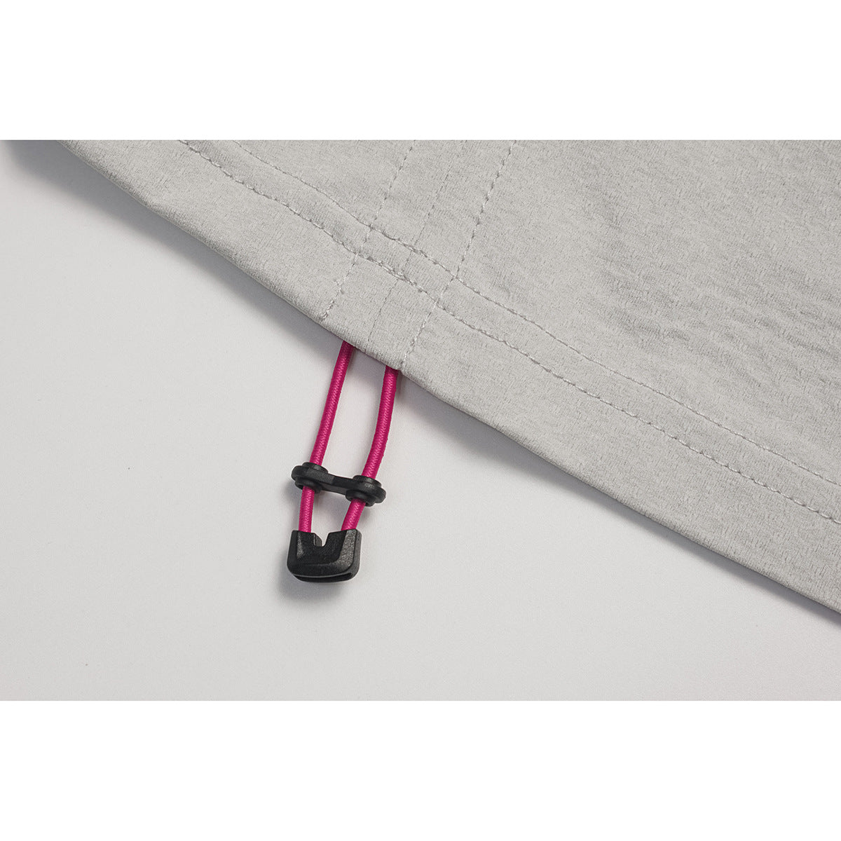 Close-up of a light gray top's hem with a bright pink adjustable drawcord and black toggle.