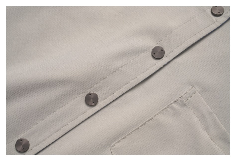 Close-up of a light taupe shirt with dark buttons along the front placket and part of a chest pocket.