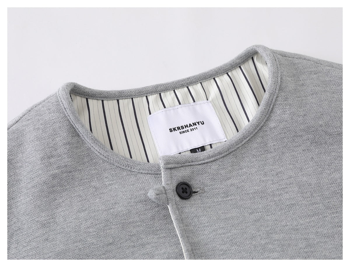 Close-up of a light gray jacket collar, striped inner lining, black button, and sewn-in neck label.