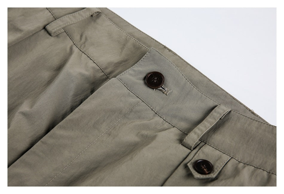 Close-up of olive-gray trouser waistband with dark buttons, buttonhole and belt loops.