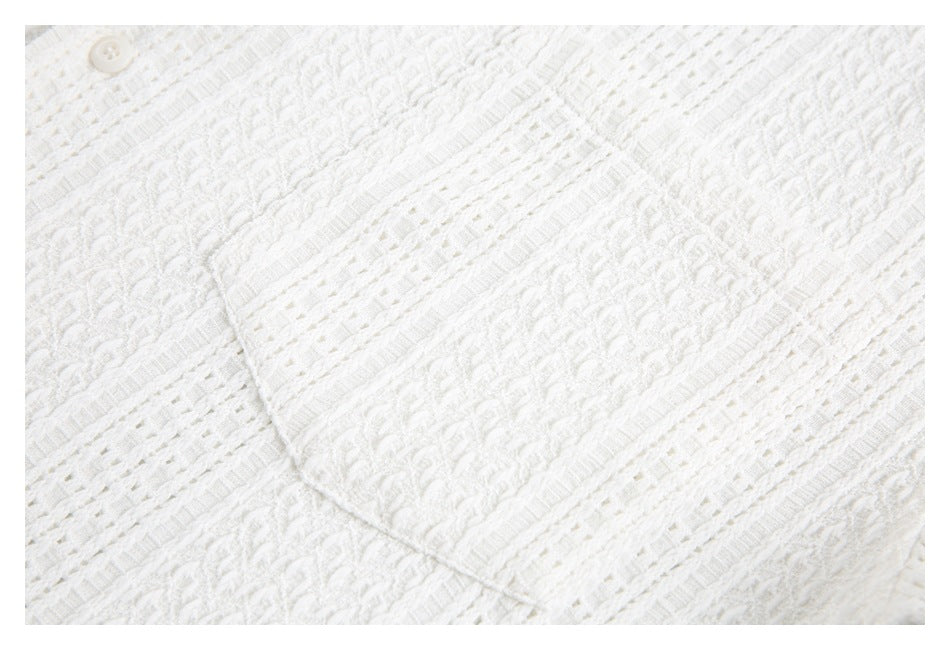 Close-up of a white textured knit garment with raised patterns, openwork stripes, and a small button.