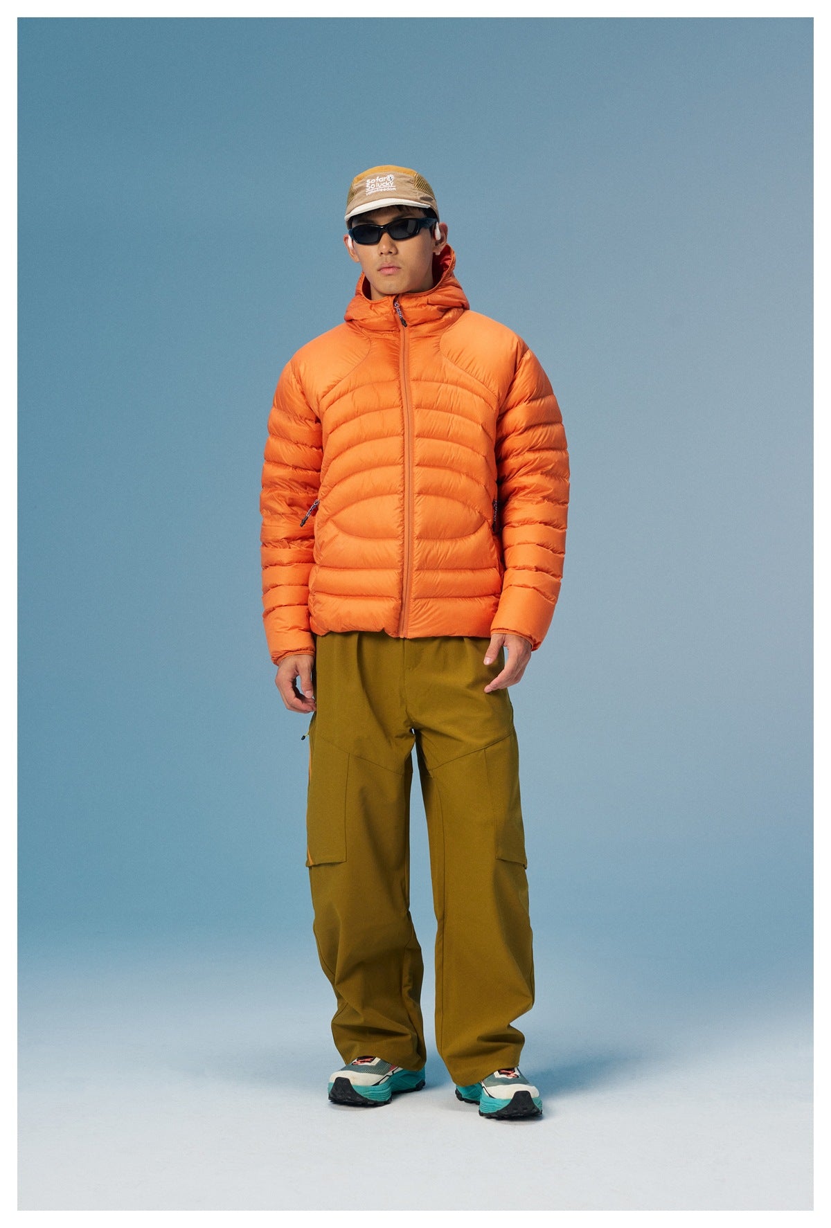 Full-length front view of a model in an orange hooded puffer jacket and olive cargo pants.