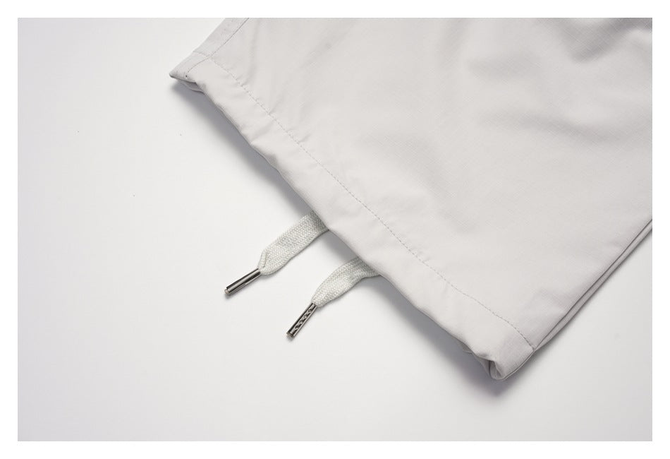 Close-up of light gray pants with white drawcords and metal tips beside a stitched edge.