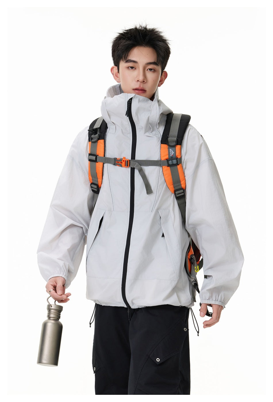 Model wearing a light gray hooded jacket with a black zipper and an orange-and-gray backpack.