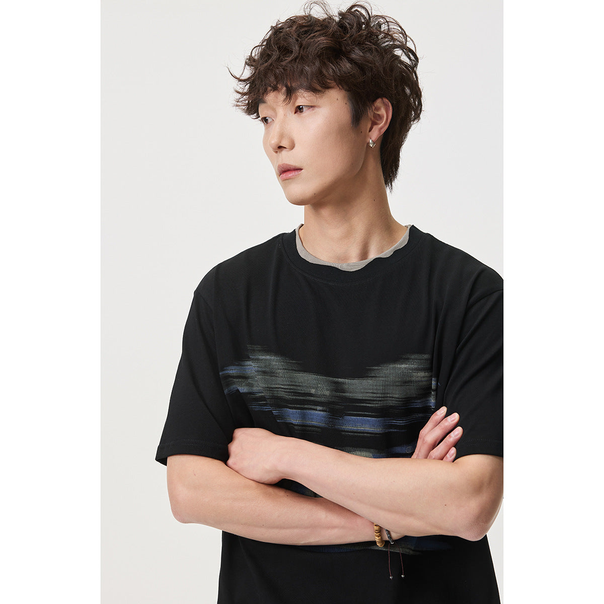 Model wearing a black short-sleeve T-shirt with an abstract gray and blue chest graphic and a layered gray neckline.