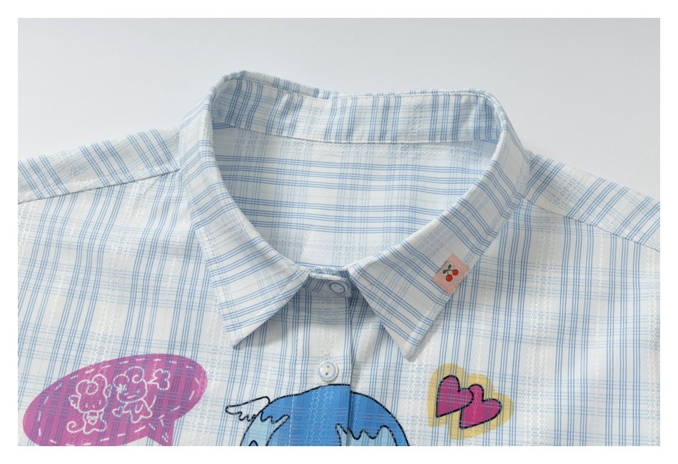 Close-up of the pale blue plaid shirt's pointed collar, buttons, and colorful chest print.