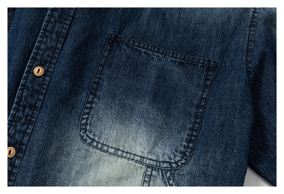 Close-up of a dark blue denim shirt's stitched chest pocket and tan buttons.