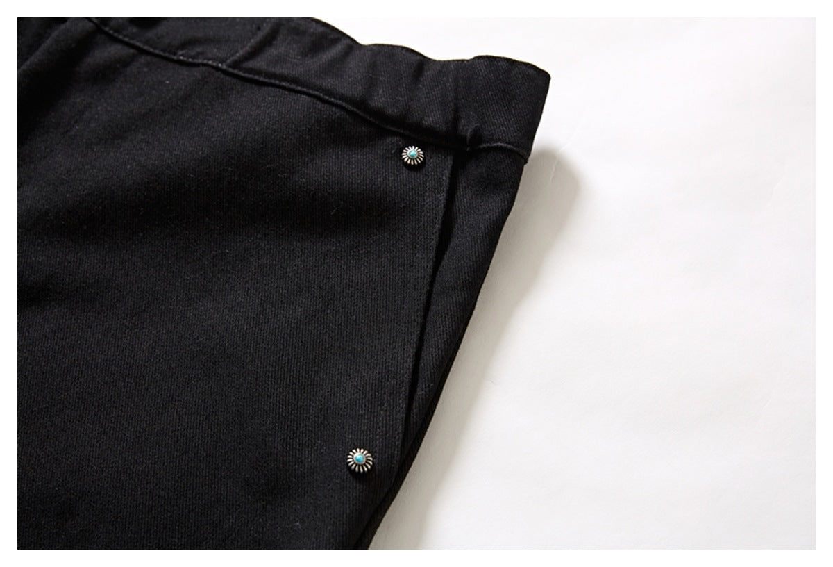 Close-up of black trousers with two small decorative buttons along a side seam.