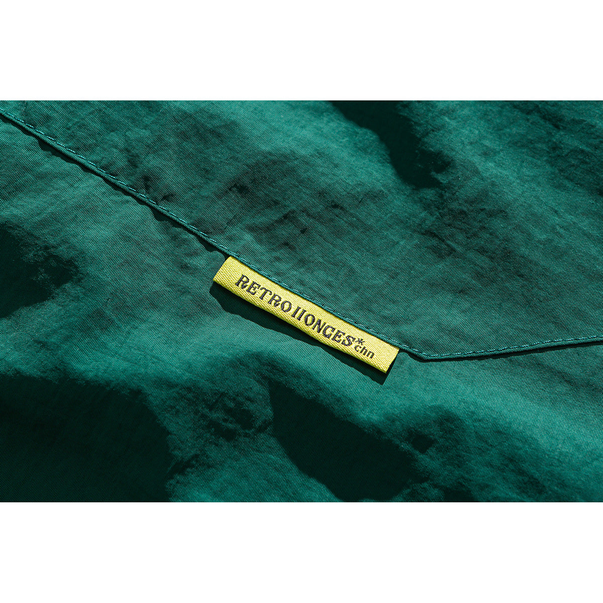 Close-up of teal fabric and seam with a small yellow sewn-in label bearing English lettering.