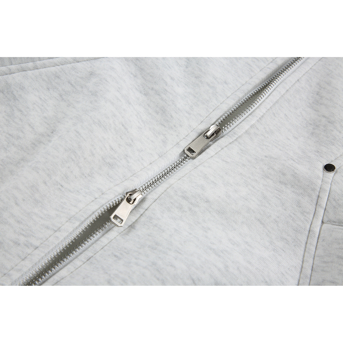 Close-up of a light gray jacket's diagonal metal zipper with two sliders.