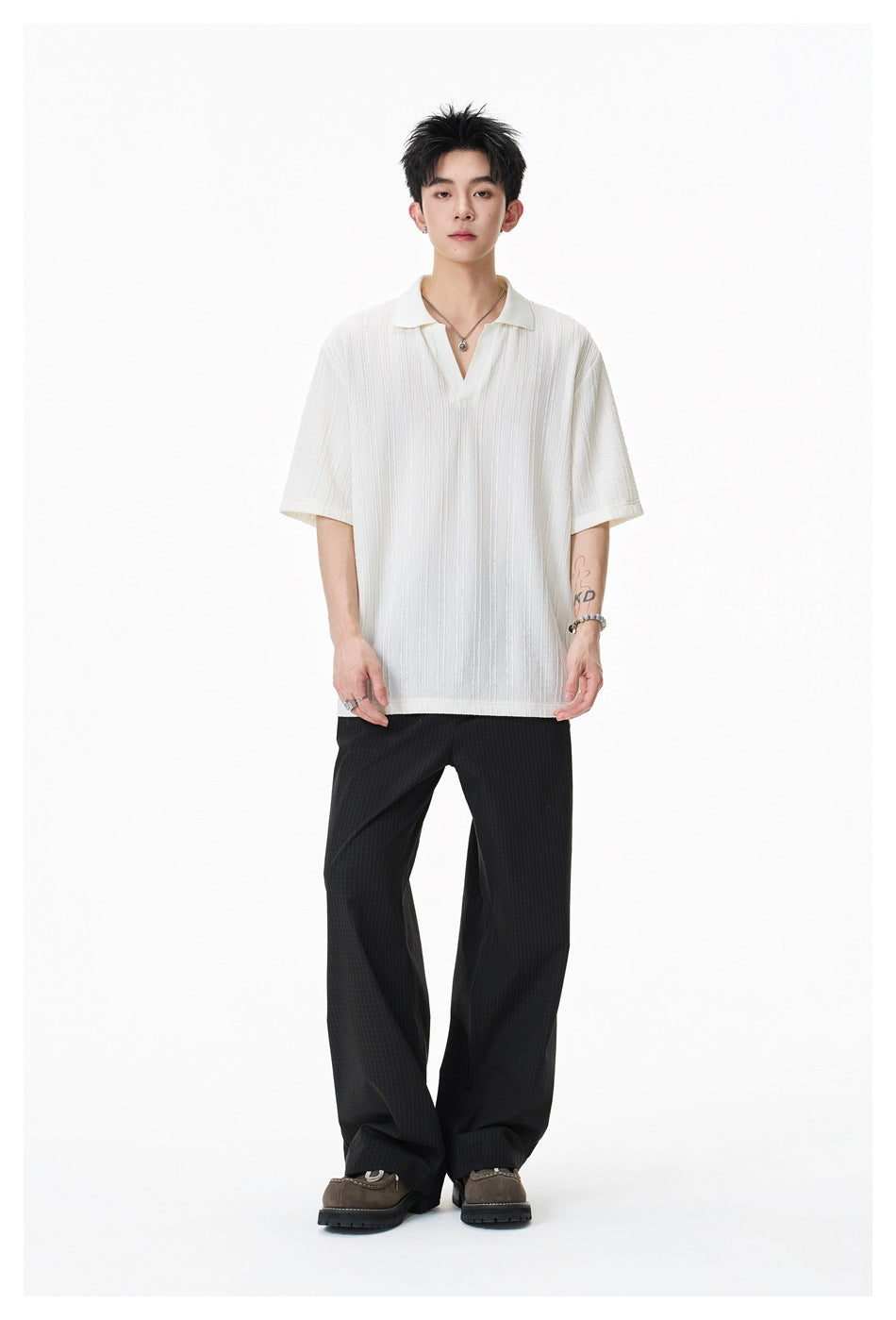 Full-length front view of a model wearing an ivory textured short-sleeve polo and wide black trousers.