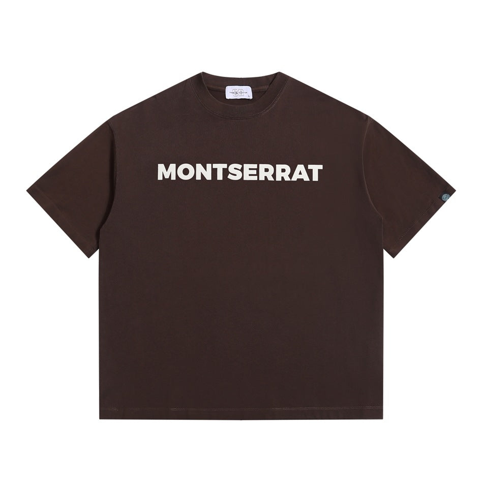 Brown short-sleeve crewneck T-shirt with white MONTSERRAT block lettering on the chest, flat lay