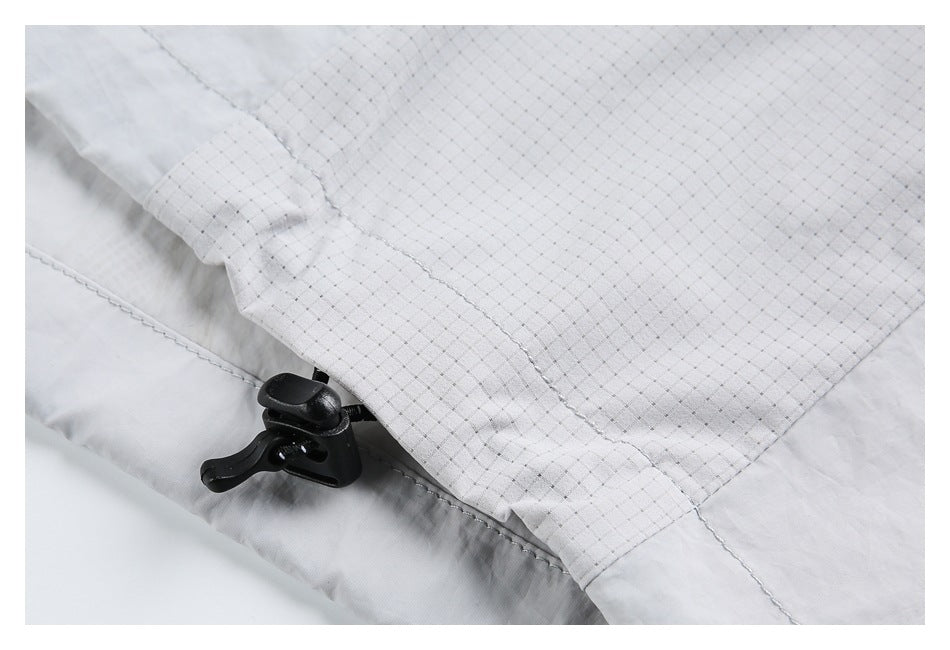 Close-up of a light gray jacket's fine grid-patterned panel and black adjustable cord toggle.