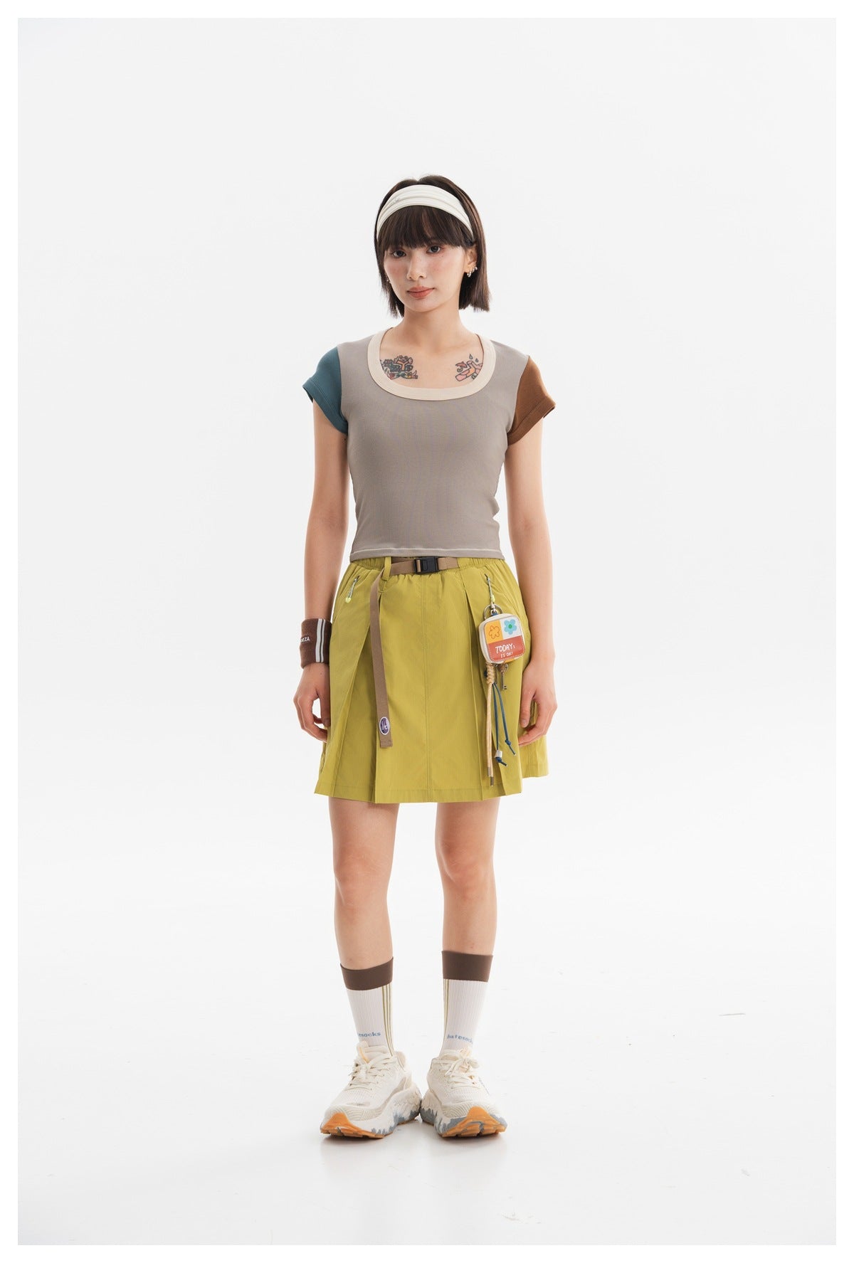 Model wearing a taupe crop top with cream neckline, teal and brown sleeves, and a lime-green skirt.