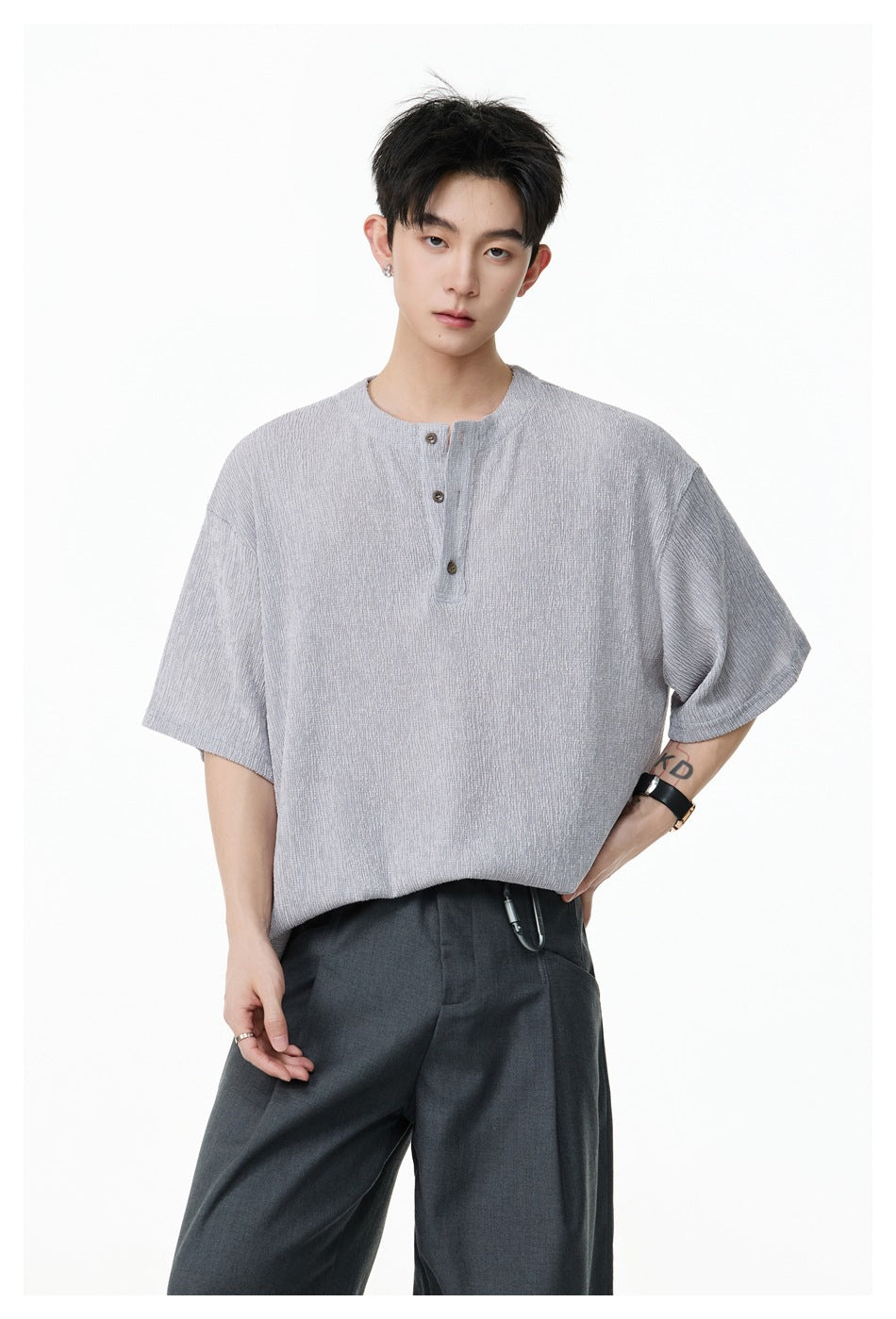 Model wearing a light gray short-sleeve Henley-collar tee with dark gray pleated trousers, front view