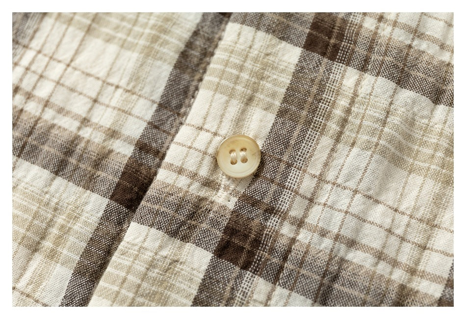 Close-up of a tan two-hole button on beige and brown plaid fabric.