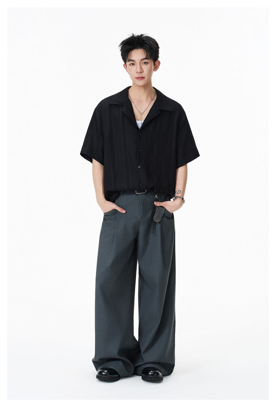 Full-length model wearing a black short-sleeve button-up shirt and wide-leg charcoal trousers.