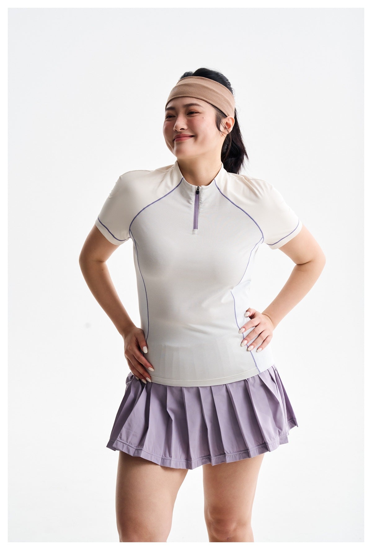 Close view of a model wearing a white short-sleeve zip top with lavender piping and a pleated lilac skirt.